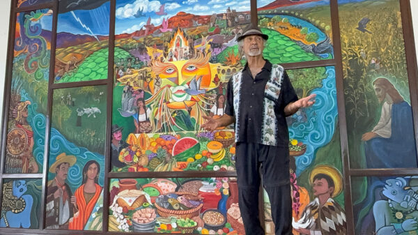 Artist Hal Marcus stands in front of a large mural he painted featuring the story of the first Thanksgiving in the United States, showcasing culture in the borderlands region of El Paso and Ciudad Juárez.
