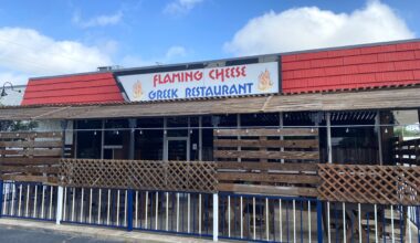 The exterior of Flaming Cheese, a Greek restaurant. There's a red awning and an enclosed patio.