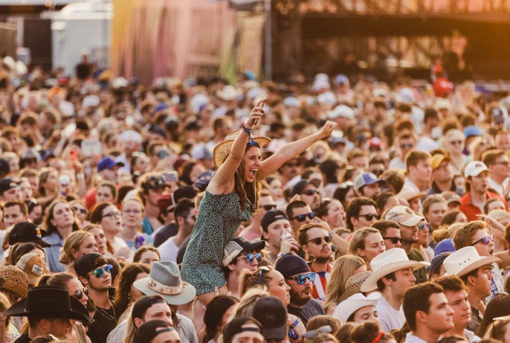 Image shows a woman raising her hands in the crowd at a festival.
