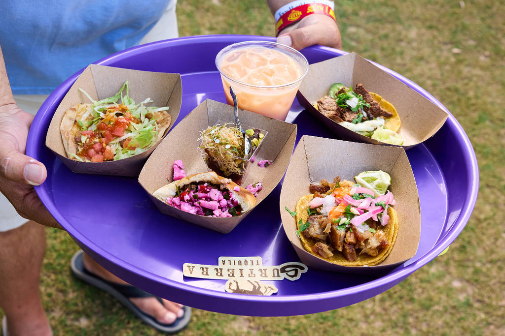 Image shows a person holding a tray of tacos. 