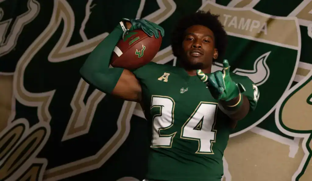 Could These 2 Sleepers Fix Dallas' Linebacker Depth? 2026 NFL Draft prospect Mac Harris of USF poses in a green Bulls uniform during a photo shoot, holding a football on his shoulder in front of a USF backdrop.