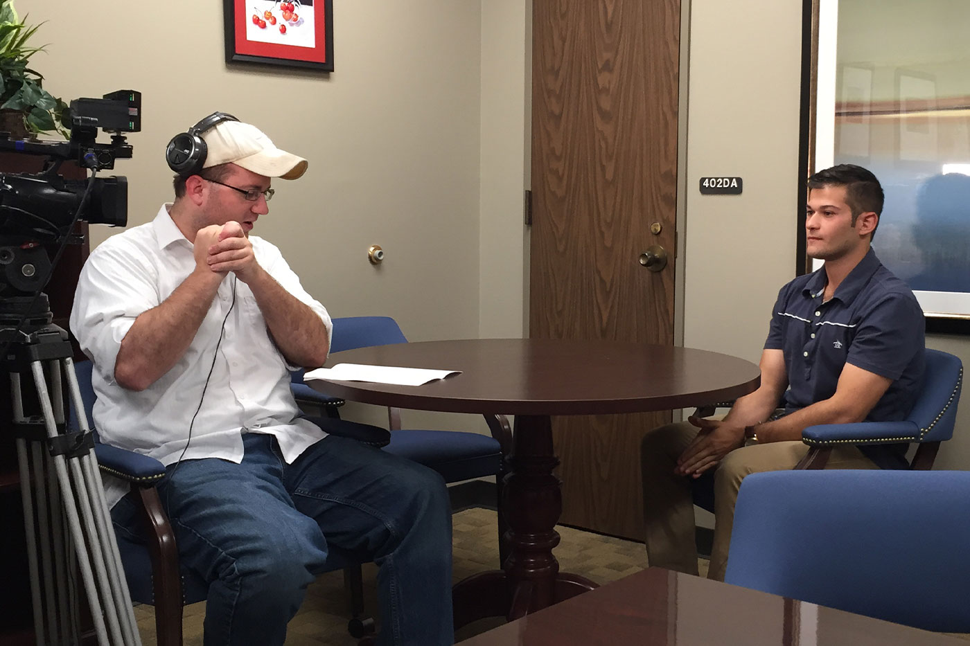 Bailey seated at a table, being interviewed on camera. 