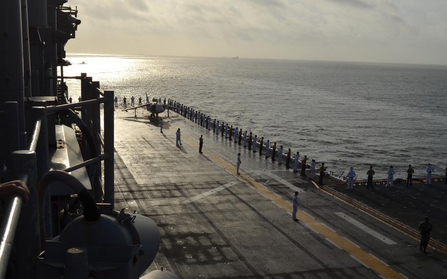Morning shines on the deck, with sailors lining the rail.