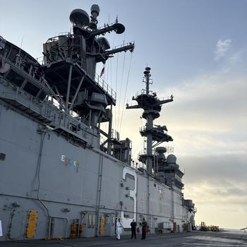 Sailors stand on the flight deck next to the island.