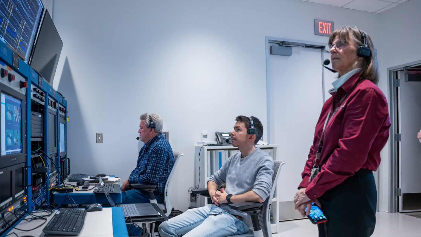Three people in a control room watching computer monitors.