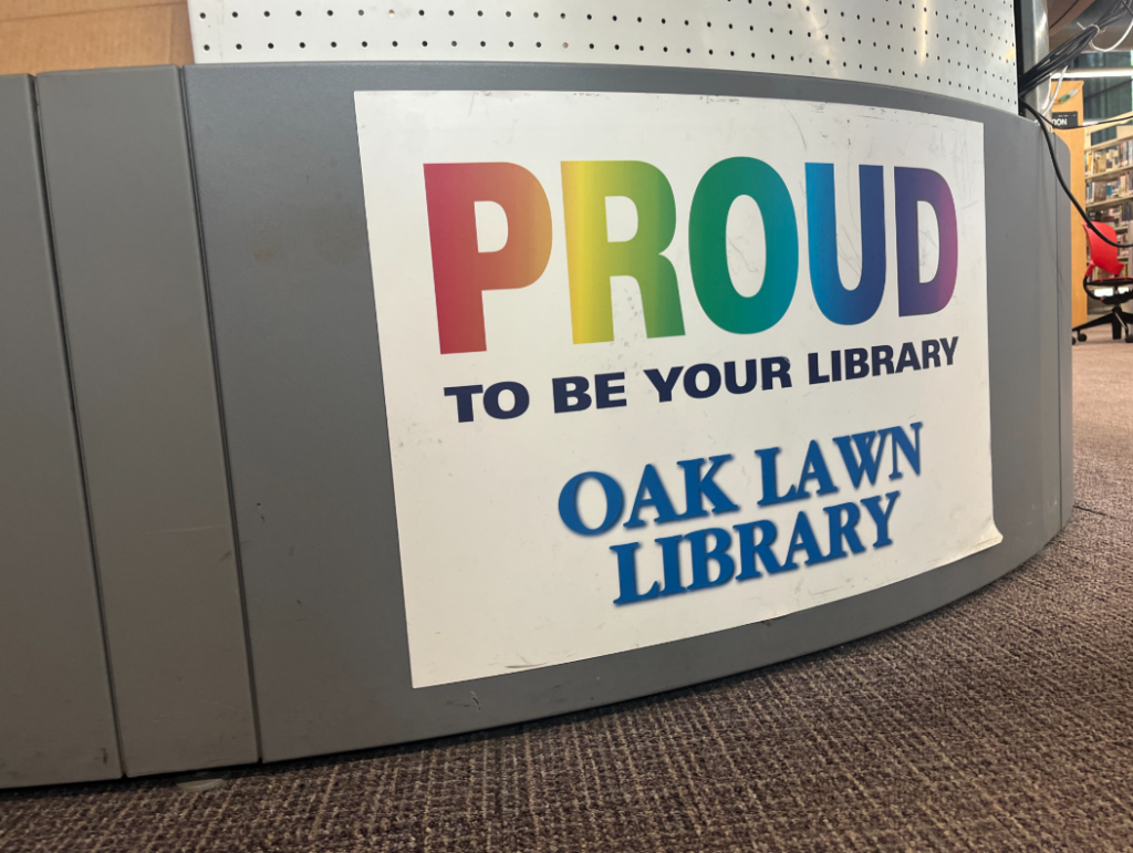 The front desk of the Oak Lawn Library tells visitors it's proud to be their library with a rainbow lettering sign.