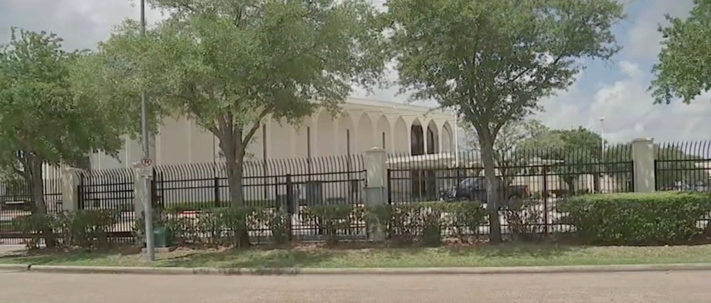Exterior of the synagogue behind a black metal fence and bushes.