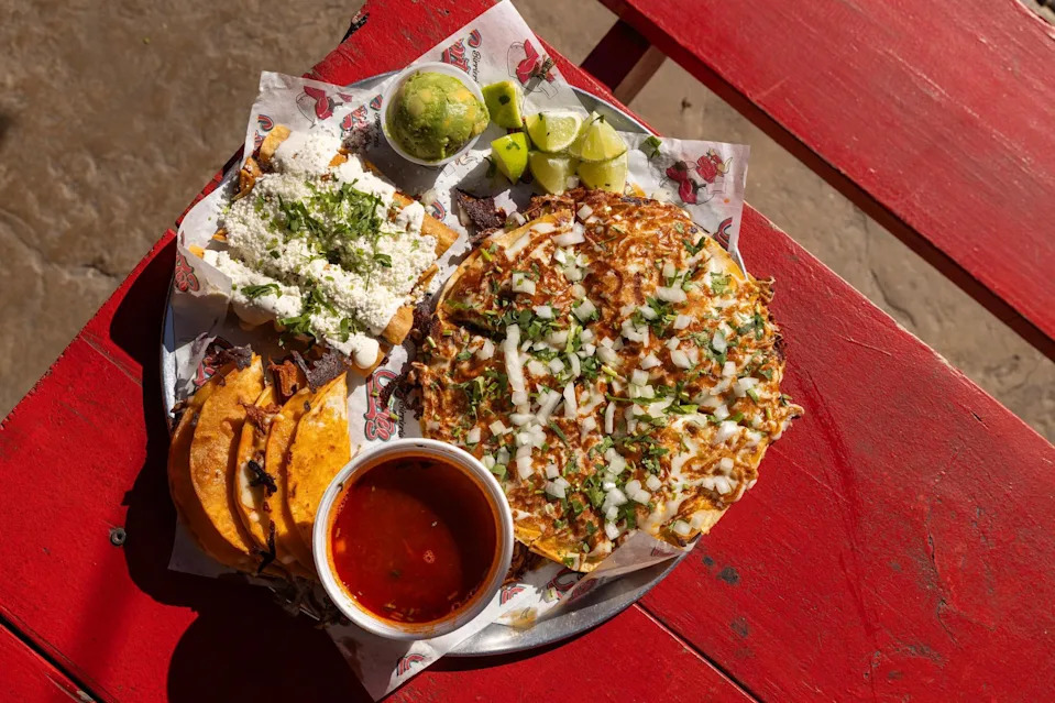 Quesatacos and consomé, bottom left, flautas, top left, and the birria pizza, right, are plated for the sampler platter at Birrieria y Taqueria Cortez in Fort Worth on Wednesday, Nov. 20, 2024. The restaurant earned a Michelin Recommended rating, landing the taqueria on a prestigious list of eateries around the nation.
