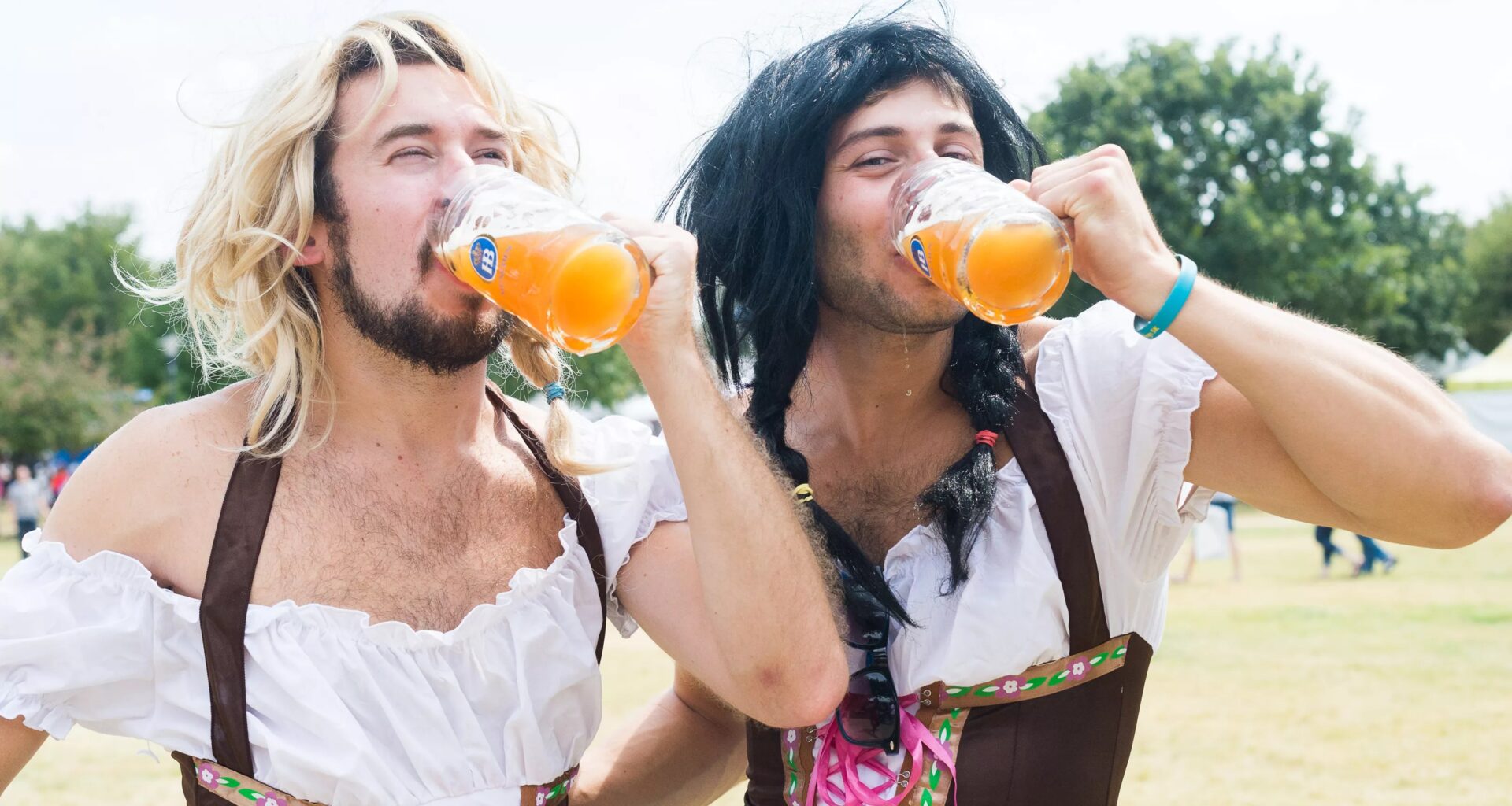 Two men wearing traditional German outfits drinking beer.