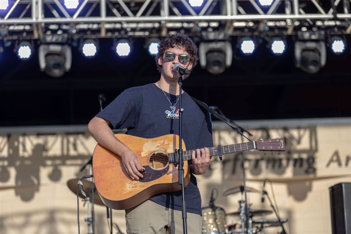Teenager holding a guitar and singing on stage at Levitt Pavilion Arlington