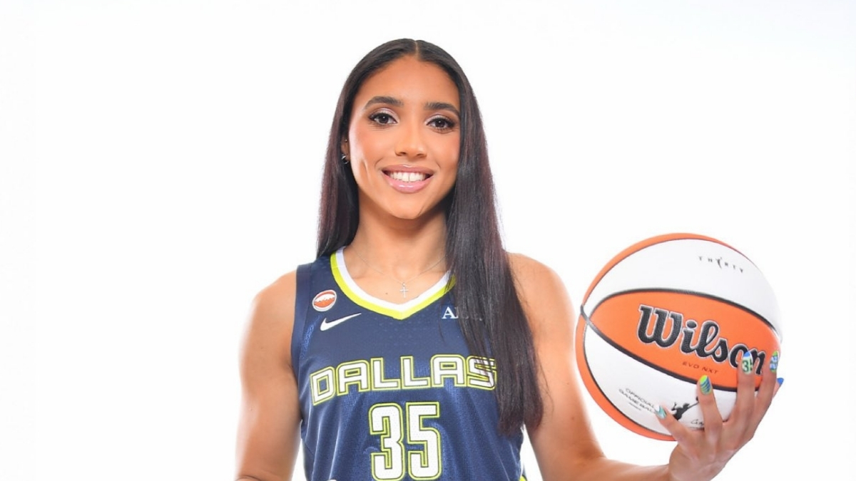 Azzi Fudd in a navy blue Dallas Wings Nike Explorer Edition jersey holding a basketball at her 2026 introductory press conference.