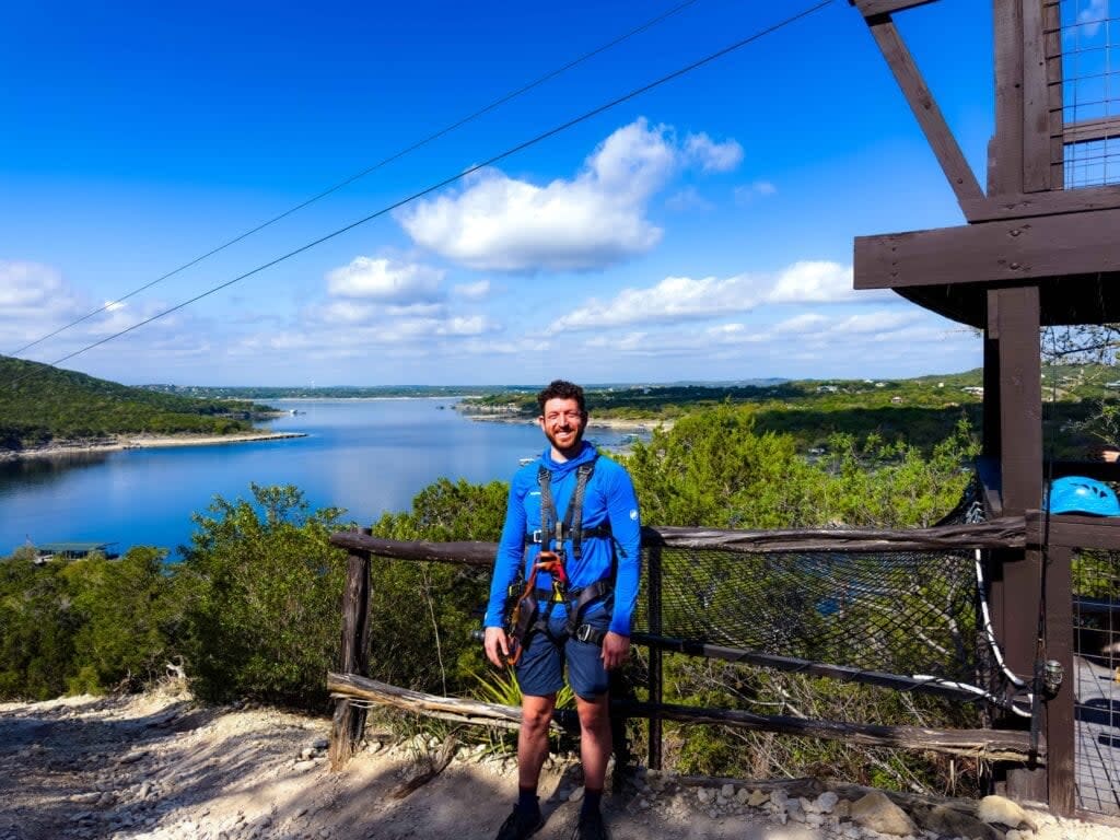 the author wearing blue in ziplining gear with lake travis in the background