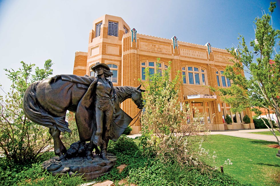 Statue of a cowboy with a horse in front of a historic building.