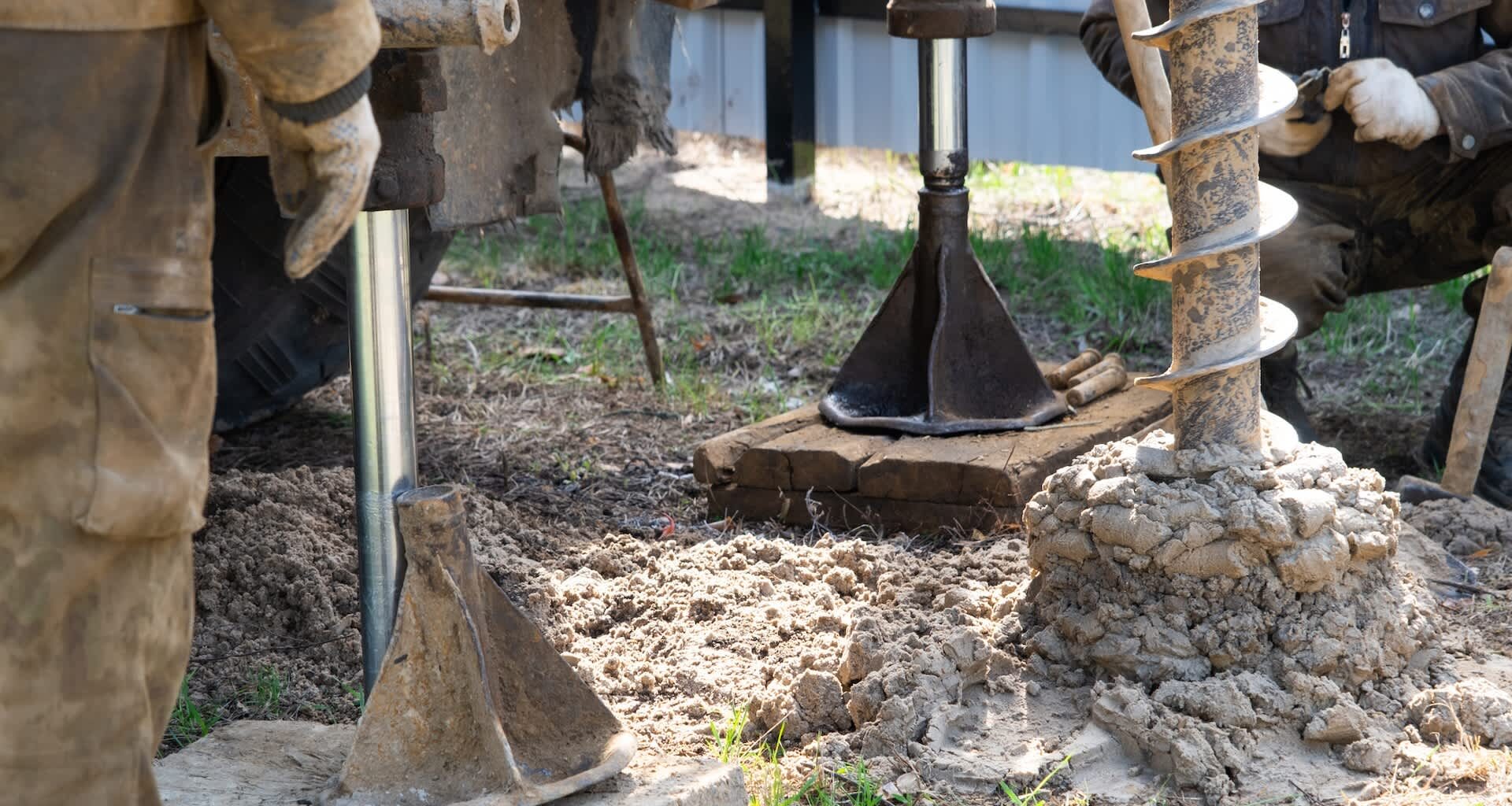Workers using heavy machinery to drill into the ground at a construction site with dirt and tools visible.
