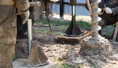 Workers using heavy machinery to drill into the ground at a construction site with dirt and tools visible.