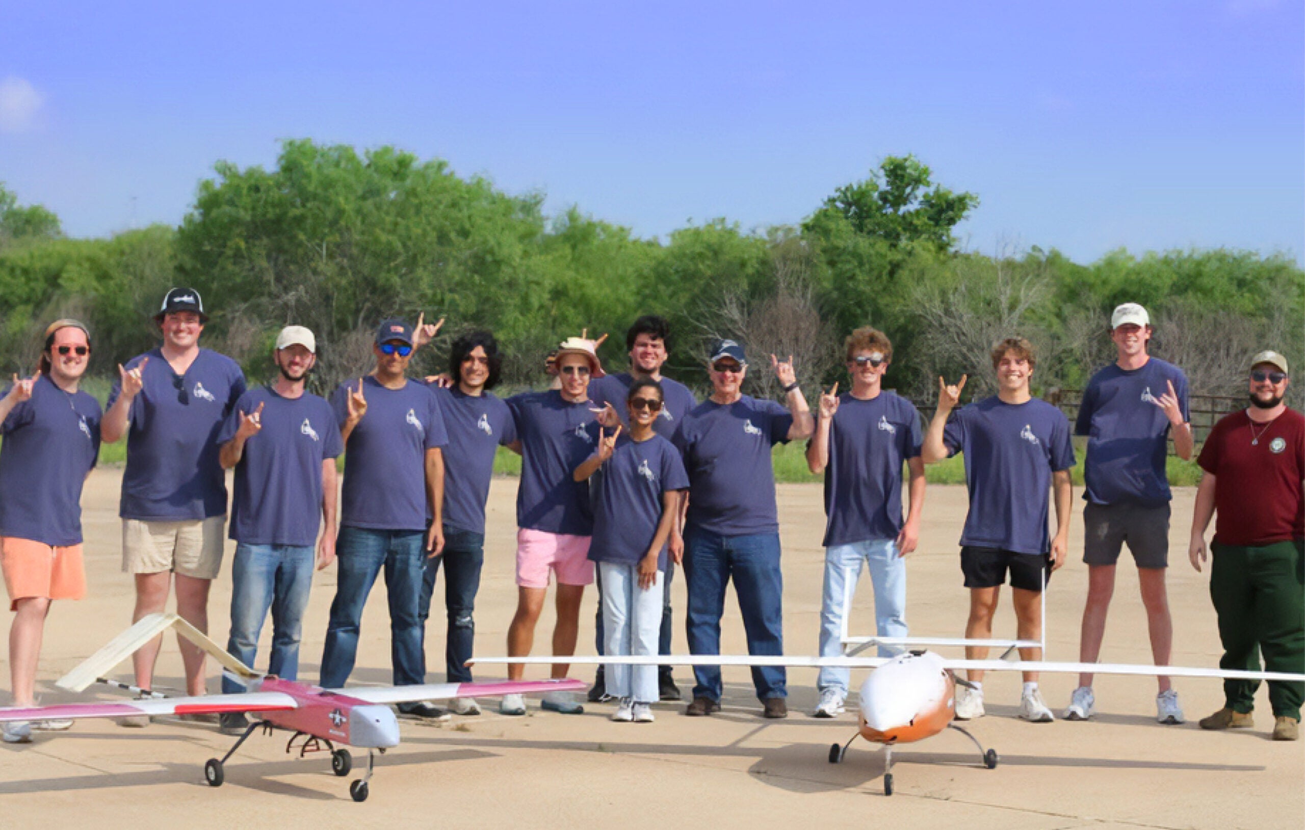 group photo of people with the hook 'em hand sign standing in front of two small aircrafts