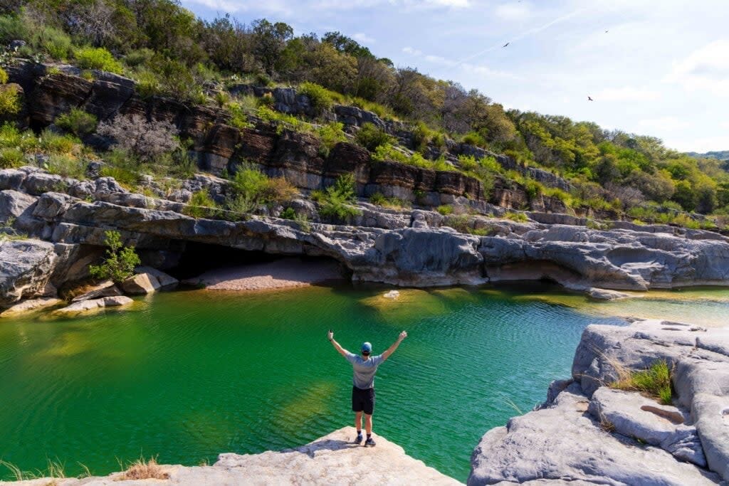 a hiker holds up his hands above the water at pedernales state park