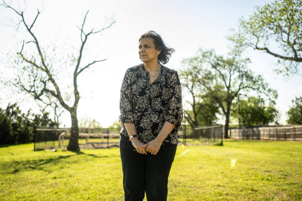 A woman stands in a field in front of an oil pipe.