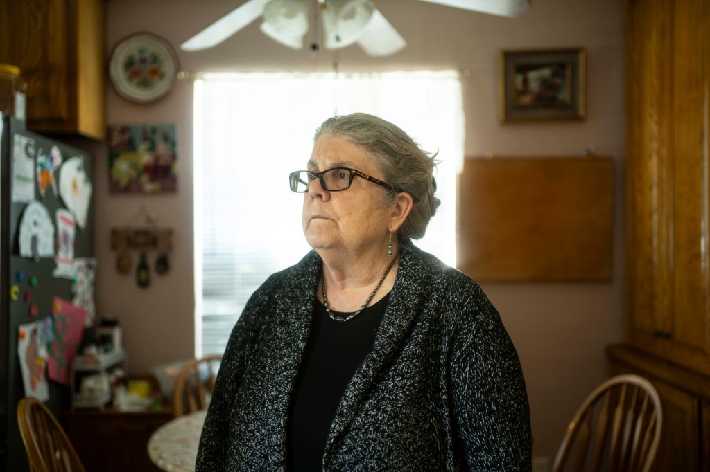 A woman stands in her kitchen looking away from the camera.