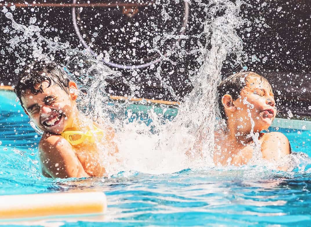 Two boys at the swimming pool splashing water and having fun. Friends playing on the water of a summer day.