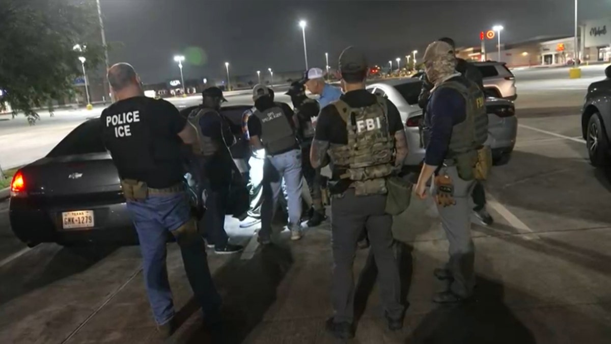ICE agents detaining a man surrounded by police officials near a car in Houston. The city is being sued by Texas Attorney General Ken Paxton over its adoption of a sanctuary ordinance.