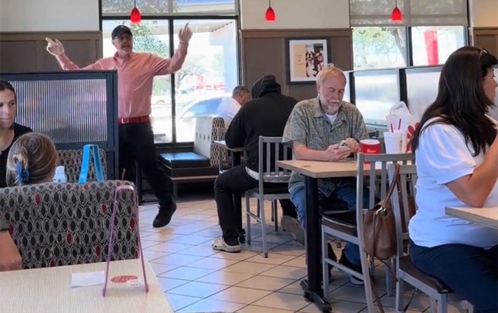 People eating in a Chick-fil-A dining room and a man in a pink shirt with his arms up