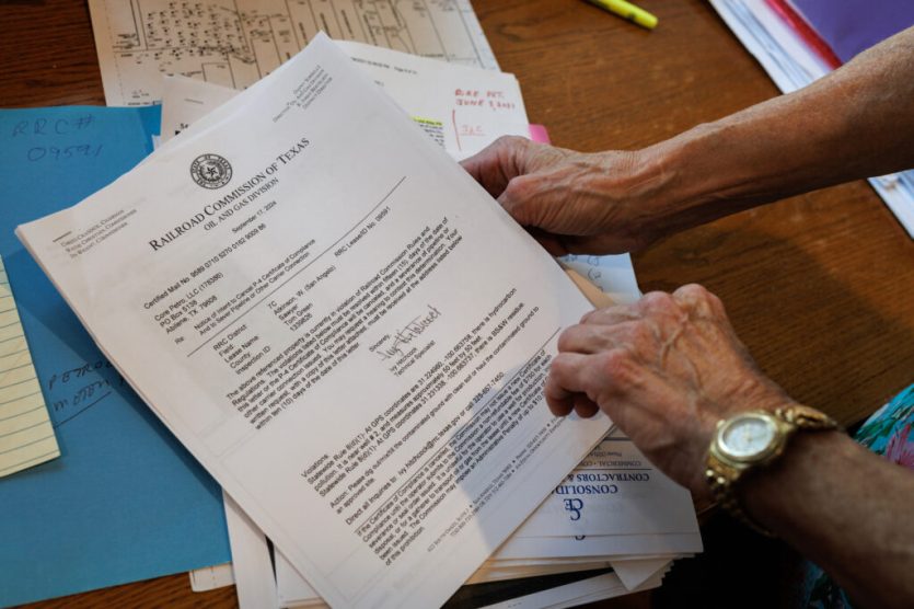 Hands flip through official documents on a wooden table top.