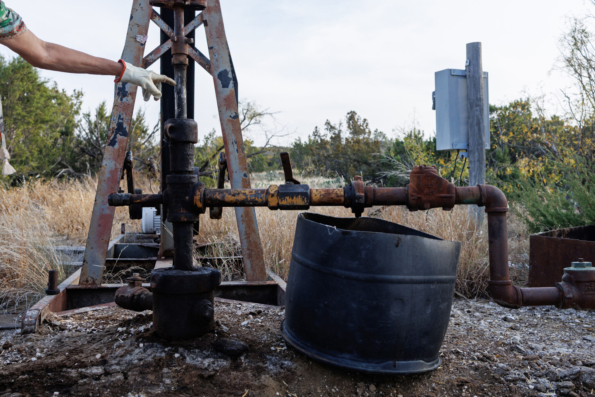 A hand in a gardening glove points to a leaking well