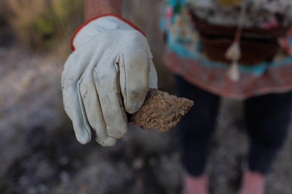 Jackie Lynn Chestnutt holds a piece of soil hardened from the produced water of an oil well, which she found next to a well on her property in Knickerbocker, Texas on Tuesday, November 18, 2025. A large number of orphan oil wells are dotted around her property, causing worry that ground water could be contaminated by leeching oil, produced water or chemicals.