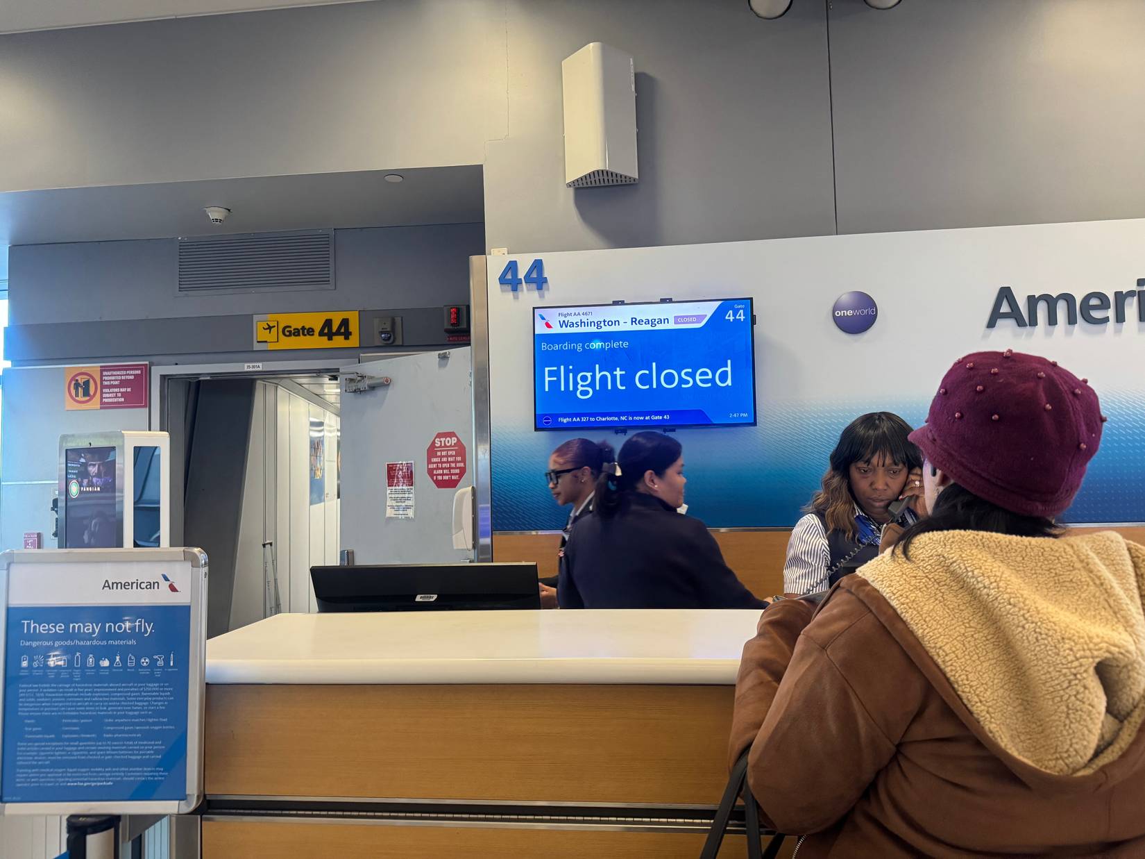 Flight information at airport gate 44 showing closed status as passengers gather near counter.