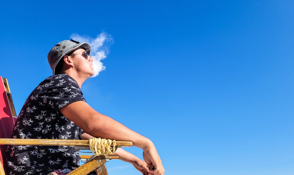 A picture of a man vaping on the beach.