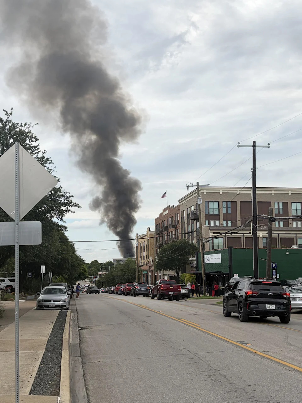 A column of thick black smoke rises above a city skyline, seen from a distance. (@MikeSirois via X)