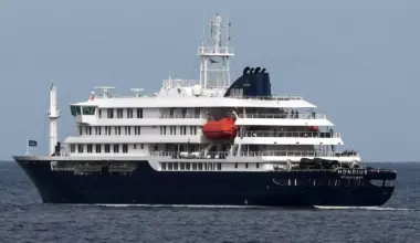 The MV Hondius cruise ship departs the port in Praia, Cape Verde. It is a large black and white cruise ship with the work "Hondius" on the end and it is in the water.