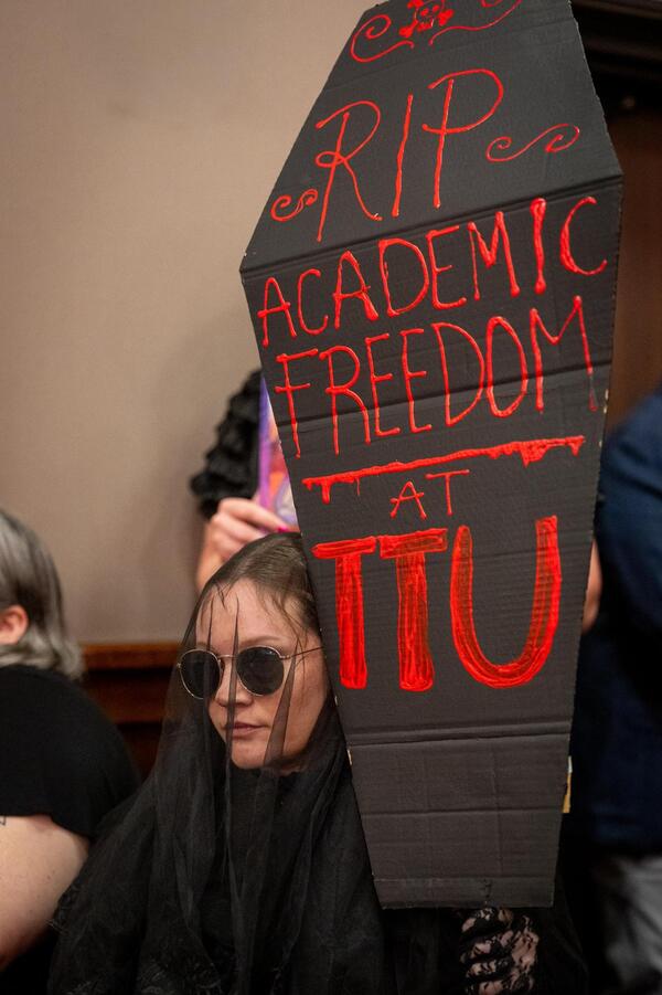 A student in a black veil holds a cardboard tombstone that says "RIP academic freedom at TTU."