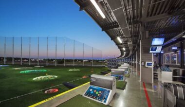 Golf driving range with electronic hitting bays and city skyline at sunset.