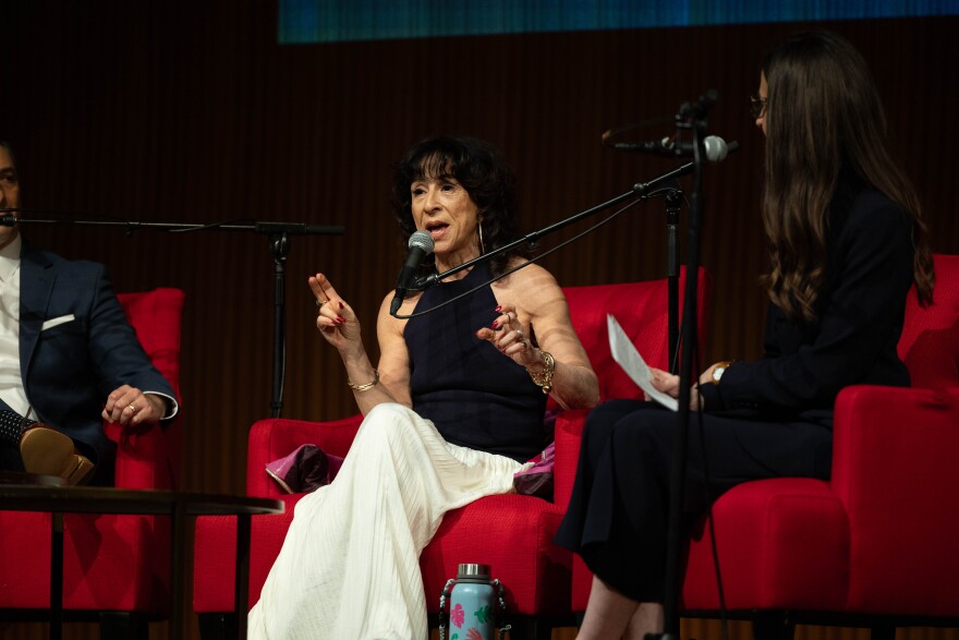 A woman sits on stage speaking into a microphone. 