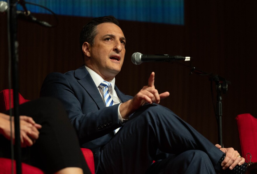 A man sitting in front of a microphone points his finger. 