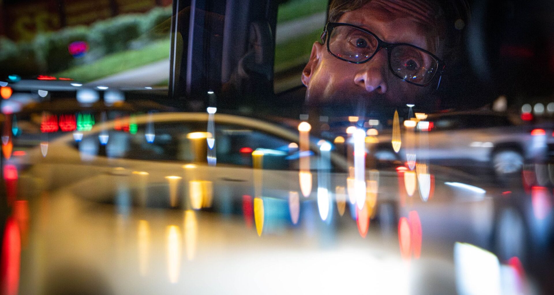 Scott Wheeler is reflected in his rearview mirror while he waits at a stoplight while delivering food in the evening in Dallas, Saturday, April 11, 2026. Traffic in the intersection is obscured using a camera lens filter.