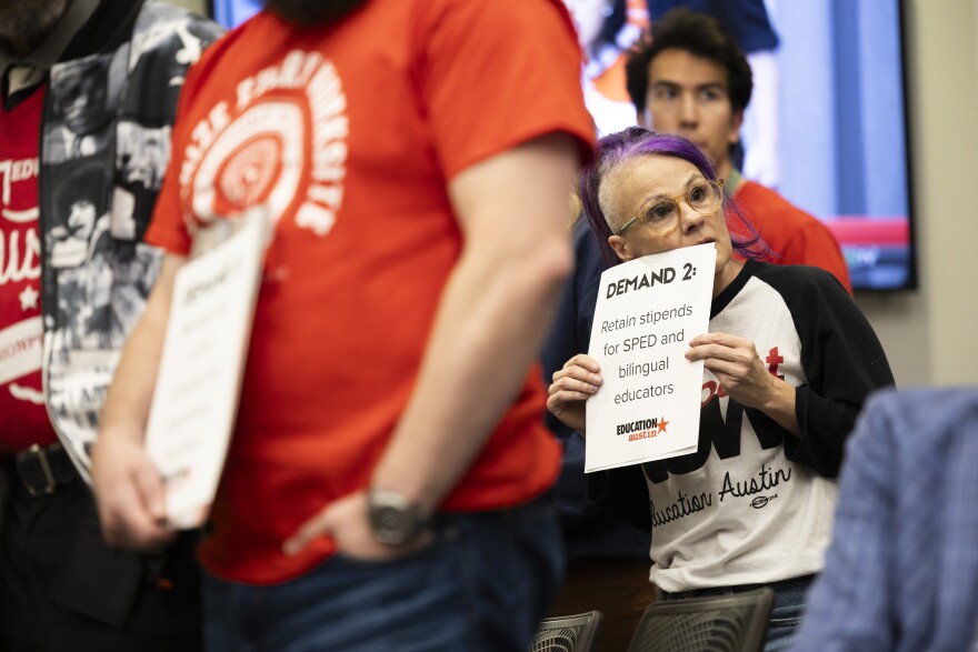 A woman holding a sign asking to retain stipends for SPED and bilingual educators looks to the sign as she stands in a crowd.
