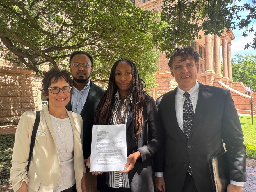 A woman holding up a paper with a another woman and man standing to her left, and another man standing to her right.