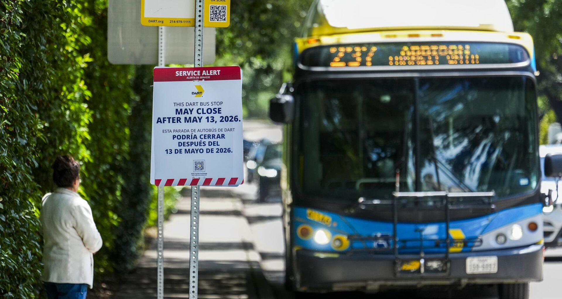 A sign warns of the possible closure of the bus stop as a woman waits for a DART route 237 bus on Preston Road at Livingston in Highland Park, Monday, May 4, 2026.