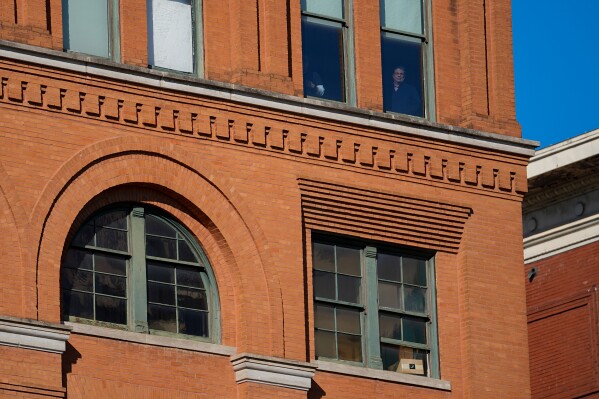 People stand at windows one floor above the 6th floor of the book depository at Dealey Plaza, on the 60th anniversary of former President John F. Kennedy's assassination, Nov. 22, 2023, in Dallas. (AP Photo/Julio Cortez, File)