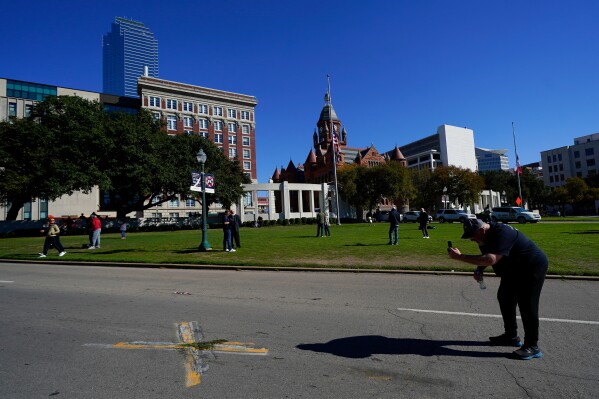 A person uses a cell phone to take pictures of an X on Elm Street at Dealey Plaza, one of two spots marked where President John F. Kennedy was shot, as people gather on the 60th anniversary of his assassination, Nov. 22, 2023, in Dallas. (AP Photo/Julio Cortez, File)
