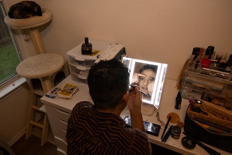 A person, seen from behind, puts on make up in a mirror.