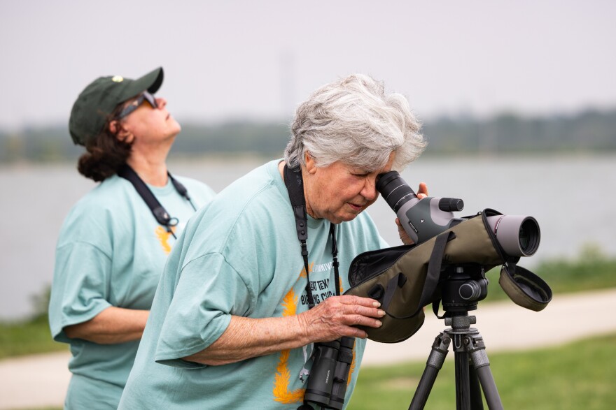 A woman looks through a scope at birds while another woman looks at the sky.