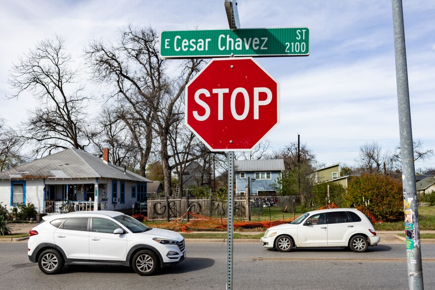 A street sign for Cesar Chavez Street is shown sitting atop a stop sign in a neighborhood.