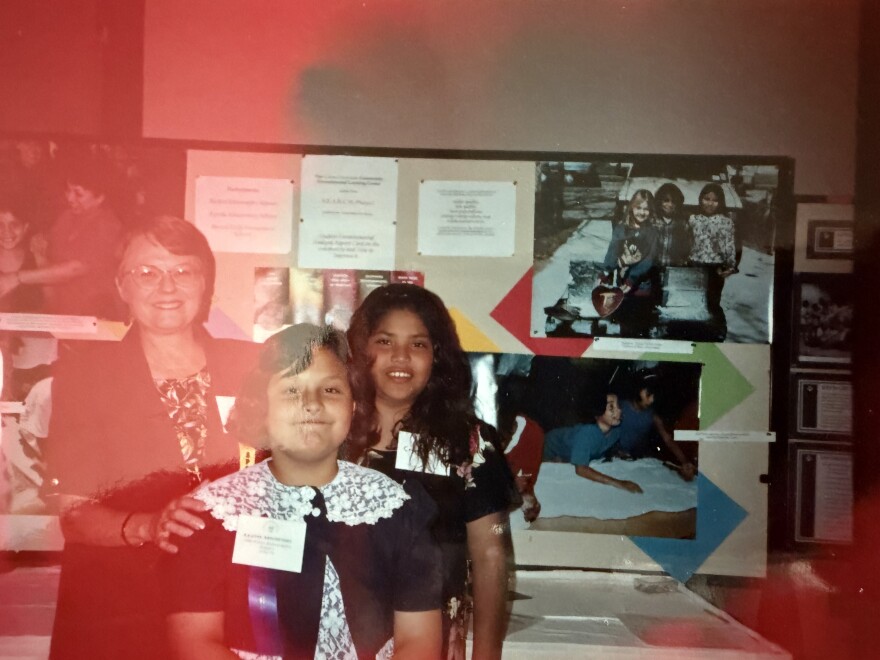Two kids and an adult standing in front of a school project with photos.