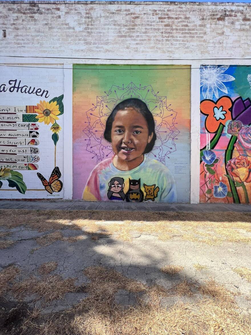 A brightly colored mural of a young girl wearing a shirt with cartoon characters. There are flowers and butterflies in the walls next to the picture of the girl.
