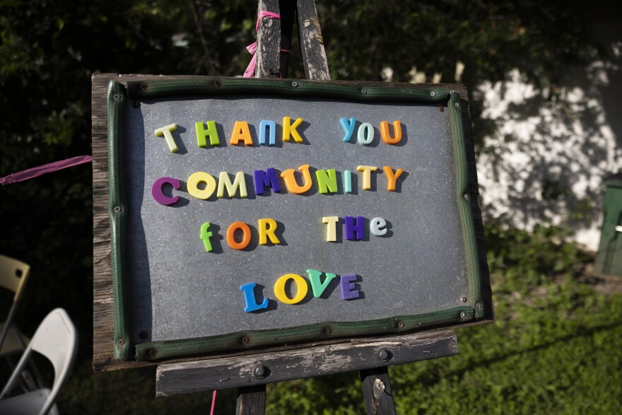 A welcome sign reading "Thank you community for the love" sits on on easel outside a home.