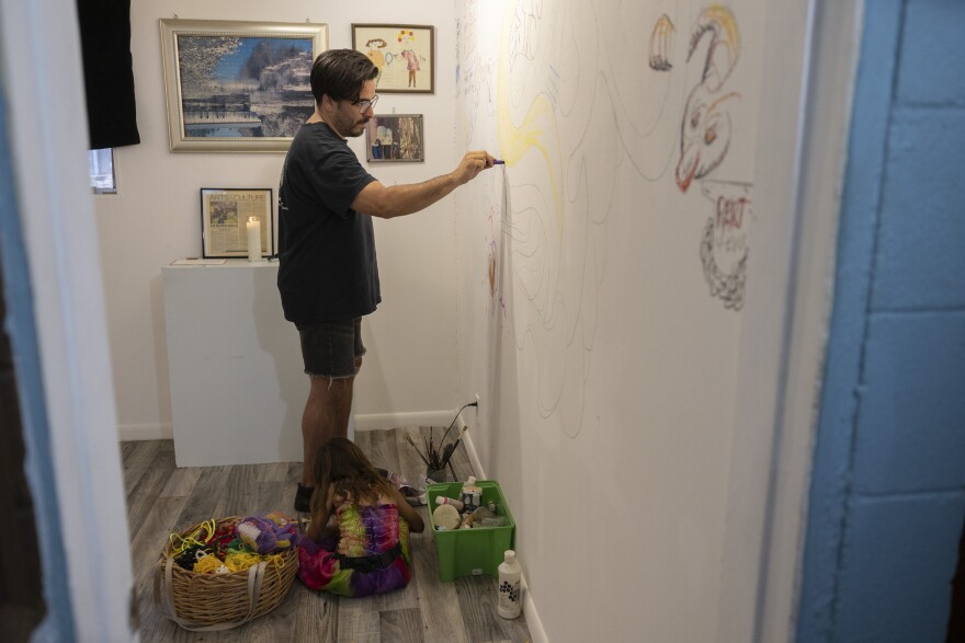 A man, standing, writes on a wall inside a home.